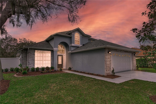 traditional-style home with driveway, stucco siding, an attached garage, a front yard, and brick siding