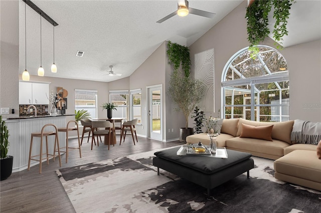 living area with visible vents, a ceiling fan, dark wood-style floors, a textured ceiling, and high vaulted ceiling