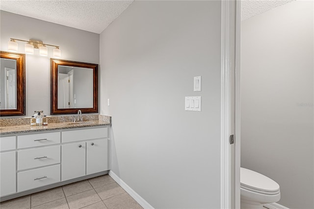 bathroom with a textured ceiling, toilet, vanity, baseboards, and tile patterned floors