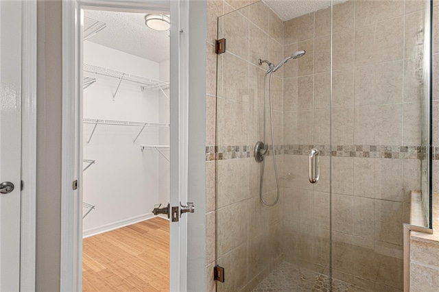 full bathroom with a textured ceiling, wood finished floors, baseboards, a shower stall, and a walk in closet