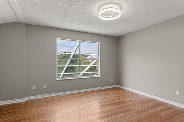 unfurnished room with a textured ceiling, light wood-type flooring, and baseboards