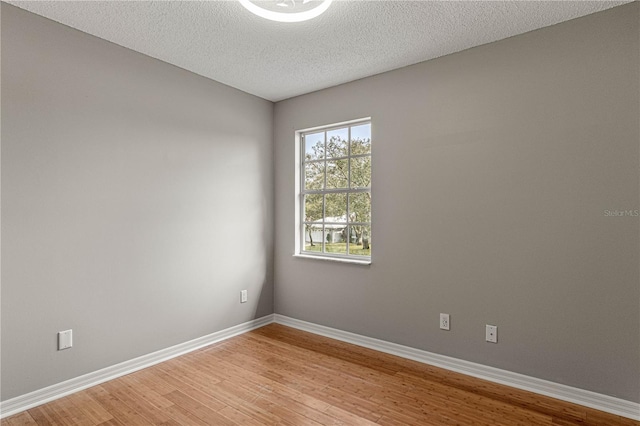 unfurnished room with a textured ceiling, light wood-type flooring, and baseboards