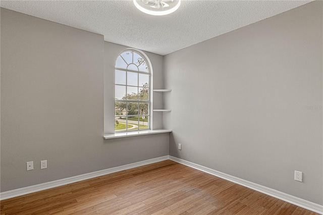 unfurnished room featuring light wood finished floors, baseboards, and a textured ceiling