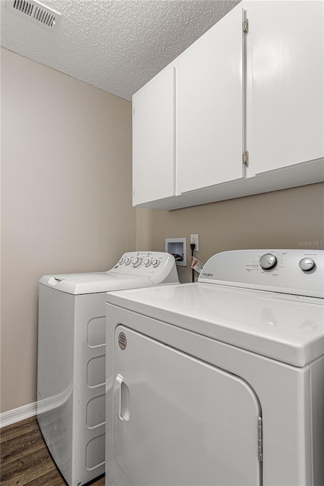 laundry room with a textured ceiling, separate washer and dryer, dark wood-type flooring, visible vents, and cabinet space