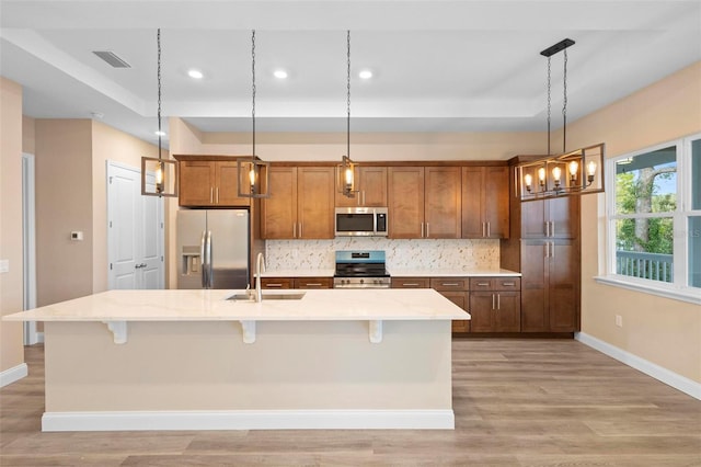 kitchen featuring stainless steel appliances, a sink, a center island with sink, and brown cabinets