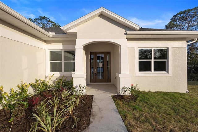 doorway to property with roof with shingles, a lawn, and stucco siding