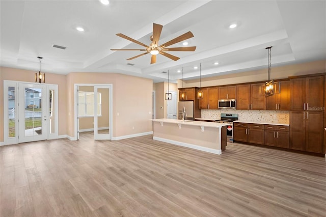 kitchen featuring stainless steel appliances, a raised ceiling, a kitchen island with sink, and decorative light fixtures