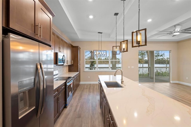 kitchen with a sink, appliances with stainless steel finishes, light stone countertops, a raised ceiling, and decorative light fixtures