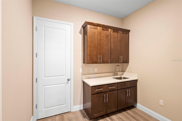 bar featuring light wood-style flooring, baseboards, and a sink