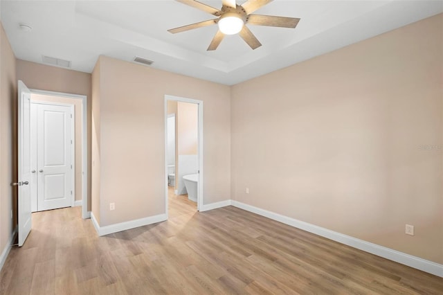 unfurnished bedroom with light wood-type flooring, a raised ceiling, visible vents, and baseboards