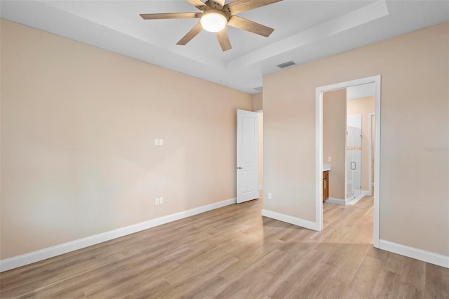 interior space featuring light wood-type flooring, a raised ceiling, visible vents, and baseboards