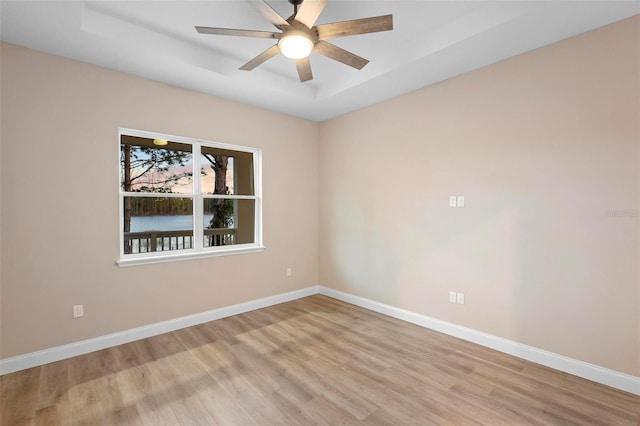 spare room with light wood-type flooring, ceiling fan, baseboards, and a raised ceiling