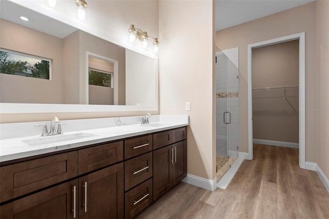 full bath featuring a stall shower, a walk in closet, a sink, and wood finished floors