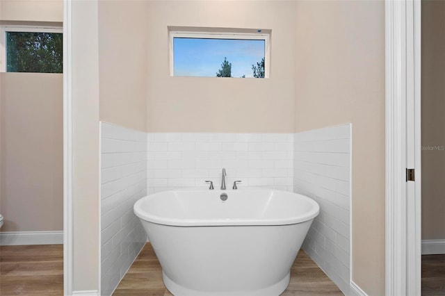 full bathroom featuring a wainscoted wall, tile walls, a freestanding bath, and wood finished floors