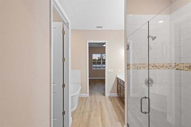 full bathroom with a stall shower, baseboards, a soaking tub, wood finished floors, and vanity