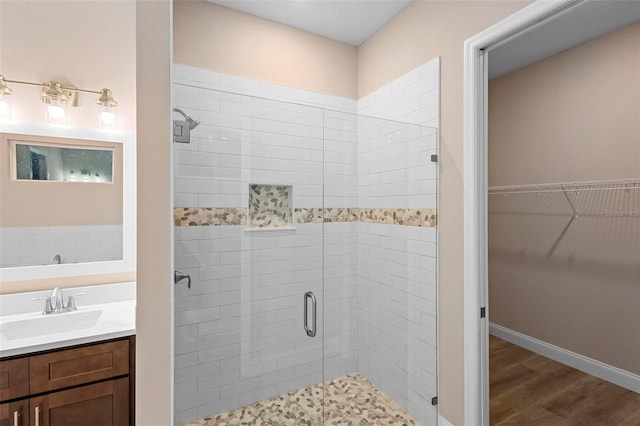 bathroom featuring wood finished floors, vanity, baseboards, a shower stall, and a walk in closet