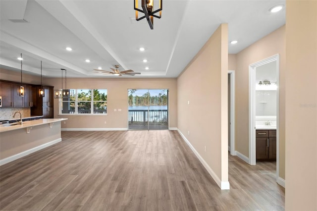 unfurnished living room featuring light wood-type flooring, baseboards, a tray ceiling, and recessed lighting