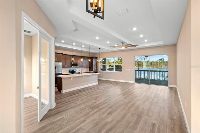 unfurnished living room with light wood-type flooring, visible vents, a tray ceiling, and baseboards