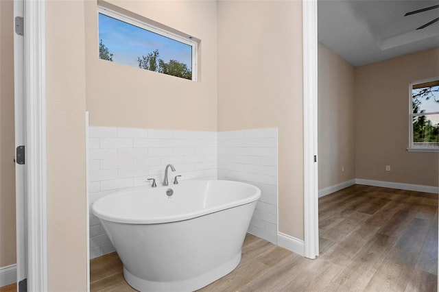 full bathroom featuring a soaking tub, tile walls, baseboards, and wood finished floors