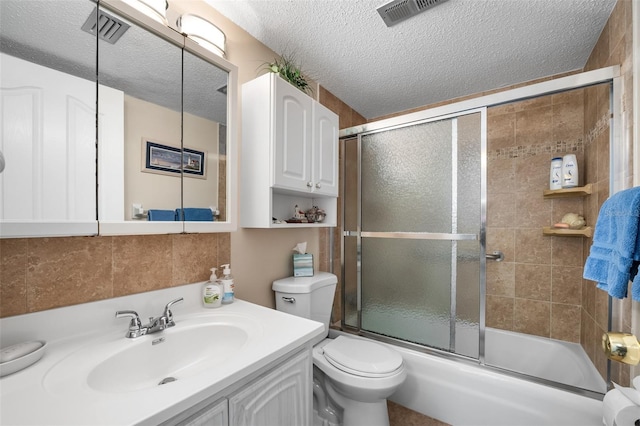 full bathroom with bath / shower combo with glass door, decorative backsplash, vanity, toilet, and a textured ceiling