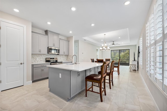 kitchen with stainless steel appliances, a kitchen island with sink, sink, and gray cabinetry