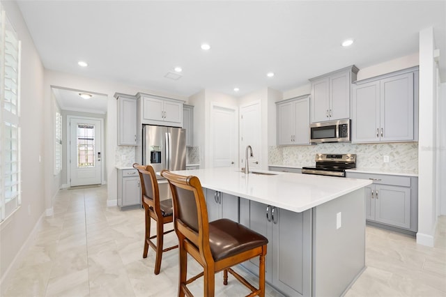 kitchen featuring a center island with sink, gray cabinets, a breakfast bar, and appliances with stainless steel finishes