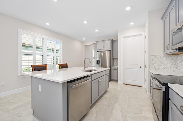 kitchen featuring appliances with stainless steel finishes, sink, a center island with sink, and gray cabinetry