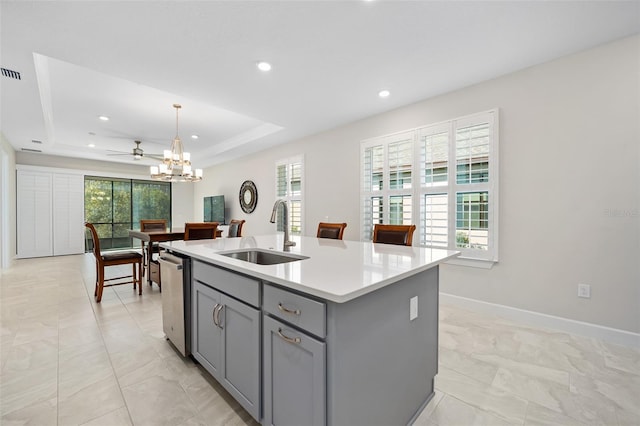 kitchen with an island with sink, sink, hanging light fixtures, a raised ceiling, and a healthy amount of sunlight