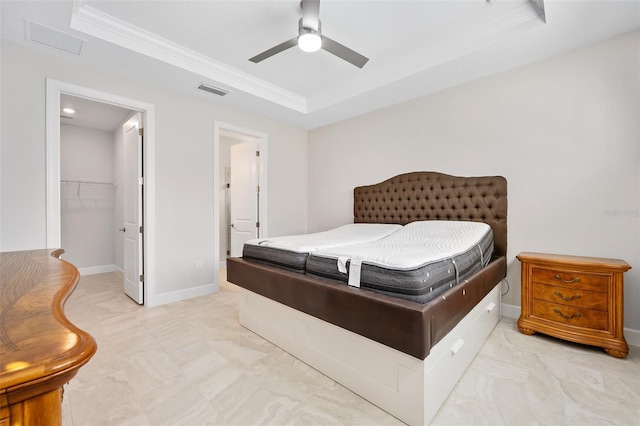 bedroom featuring ornamental molding, a walk in closet, ceiling fan, a tray ceiling, and a closet