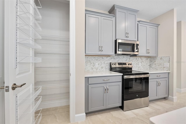 kitchen with tasteful backsplash, appliances with stainless steel finishes, and gray cabinetry