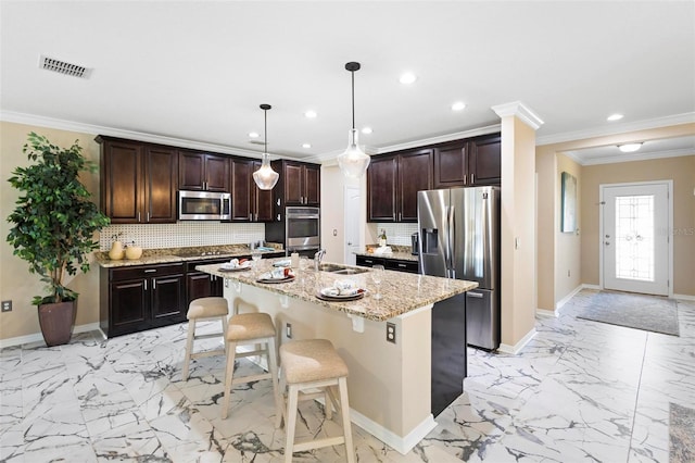 kitchen featuring pendant lighting, sink, appliances with stainless steel finishes, a kitchen island with sink, and a kitchen bar