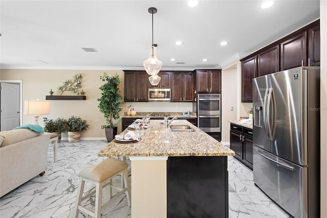 kitchen featuring appliances with stainless steel finishes, sink, a kitchen bar, hanging light fixtures, and a kitchen island with sink