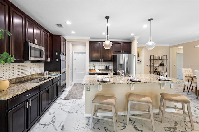 kitchen featuring appliances with stainless steel finishes, a kitchen bar, hanging light fixtures, light stone countertops, and a center island with sink