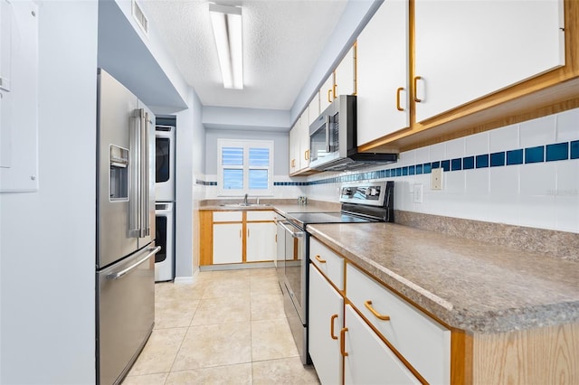 kitchen with tasteful backsplash, appliances with stainless steel finishes, a textured ceiling, a sink, and light tile patterned flooring