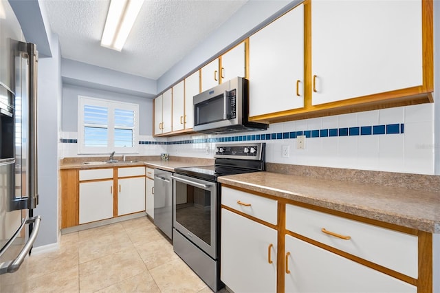 kitchen featuring backsplash, appliances with stainless steel finishes, light tile patterned flooring, a sink, and a textured ceiling