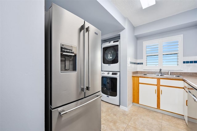 kitchen featuring light tile patterned flooring, oven, a sink, stacked washer / drying machine, and stainless steel refrigerator with ice dispenser