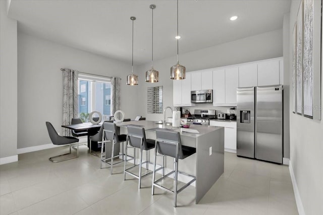 kitchen with a kitchen bar, an island with sink, pendant lighting, stainless steel appliances, and white cabinets