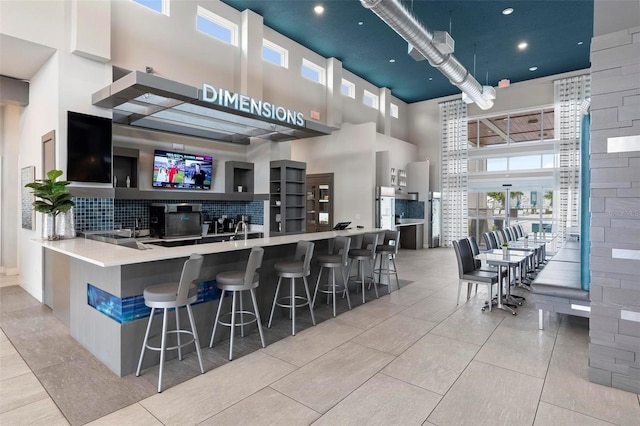 kitchen with light tile patterned flooring, a breakfast bar, kitchen peninsula, a towering ceiling, and decorative backsplash