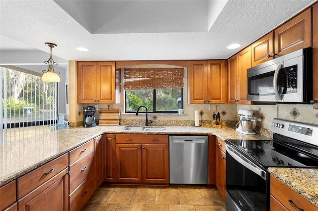 kitchen with pendant lighting, sink, light stone countertops, and appliances with stainless steel finishes