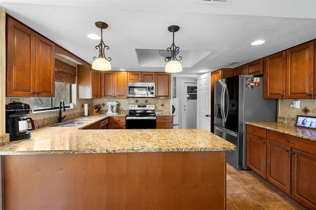 kitchen featuring sink, decorative light fixtures, appliances with stainless steel finishes, a tray ceiling, and kitchen peninsula