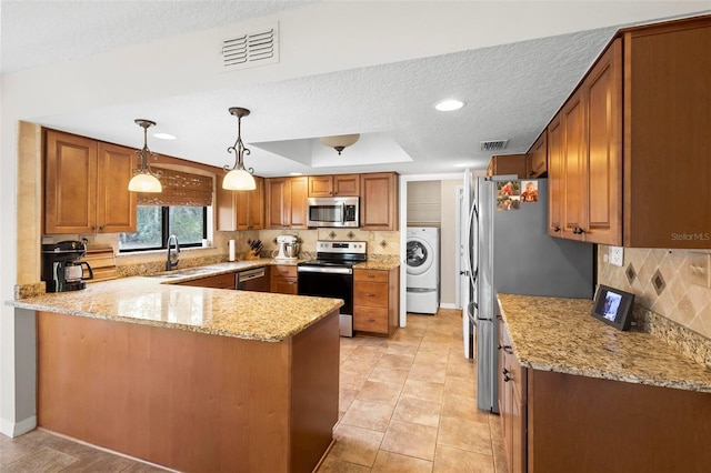 kitchen with washer / dryer, decorative light fixtures, appliances with stainless steel finishes, kitchen peninsula, and light stone countertops