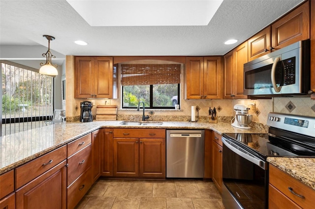 kitchen with pendant lighting, sink, appliances with stainless steel finishes, light stone counters, and decorative backsplash