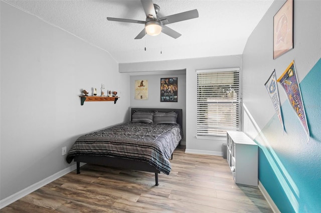 bedroom featuring ceiling fan, hardwood / wood-style flooring, vaulted ceiling, and a textured ceiling