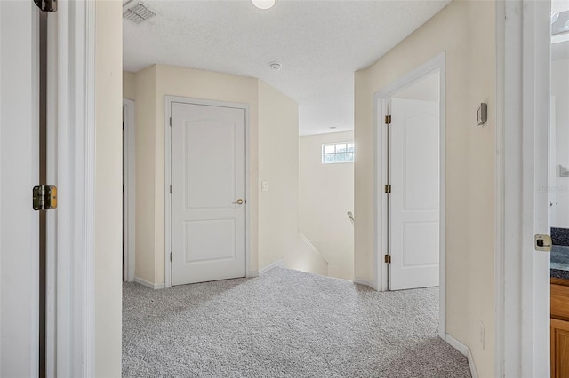 hallway featuring light colored carpet and a textured ceiling