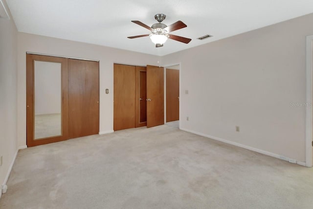 unfurnished bedroom featuring multiple closets, light carpet, and ceiling fan