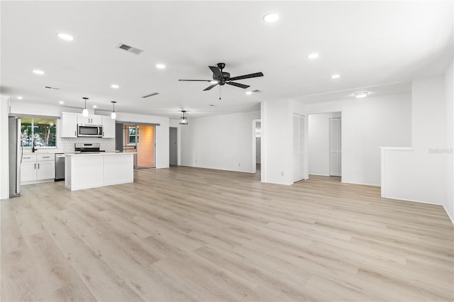 unfurnished living room with sink, ceiling fan, and light wood-type flooring