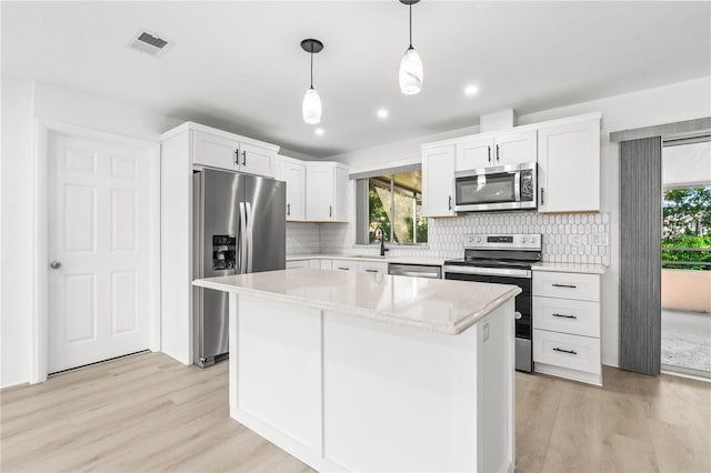 kitchen with pendant lighting, a kitchen island, white cabinets, and appliances with stainless steel finishes