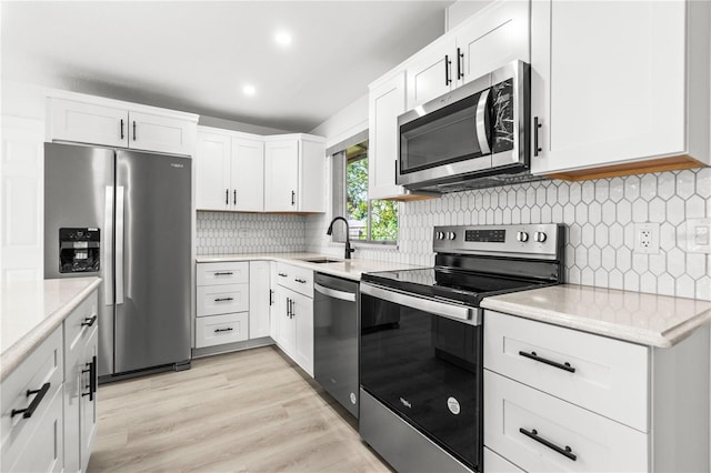 kitchen with appliances with stainless steel finishes, sink, white cabinets, decorative backsplash, and light hardwood / wood-style flooring