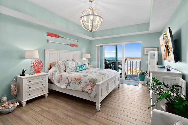 bedroom featuring a notable chandelier, a tray ceiling, and access to outside