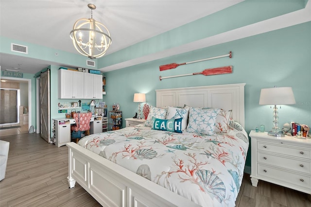 bedroom featuring a barn door, hardwood / wood-style floors, and a notable chandelier